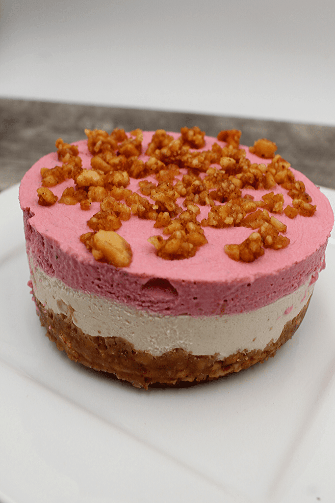 Creamy vegan and keto cheesecake with a strawberry layer and a crunchy nut base..