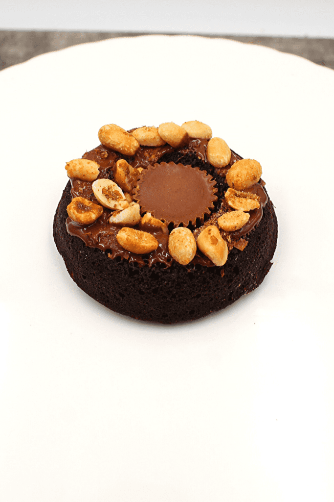 A keto chocolate doughnut with peanut butter frosting and chopped nuts on top.