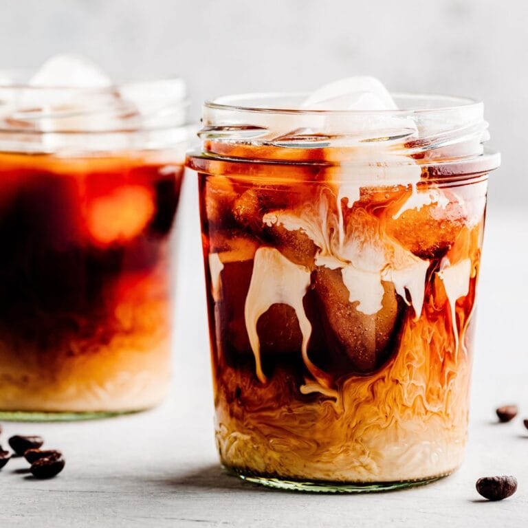 glass cups fille with ice, coffee, heavy cream and homemade sugar-free vanilla coffee syrup with espresso beans scattered around glasses