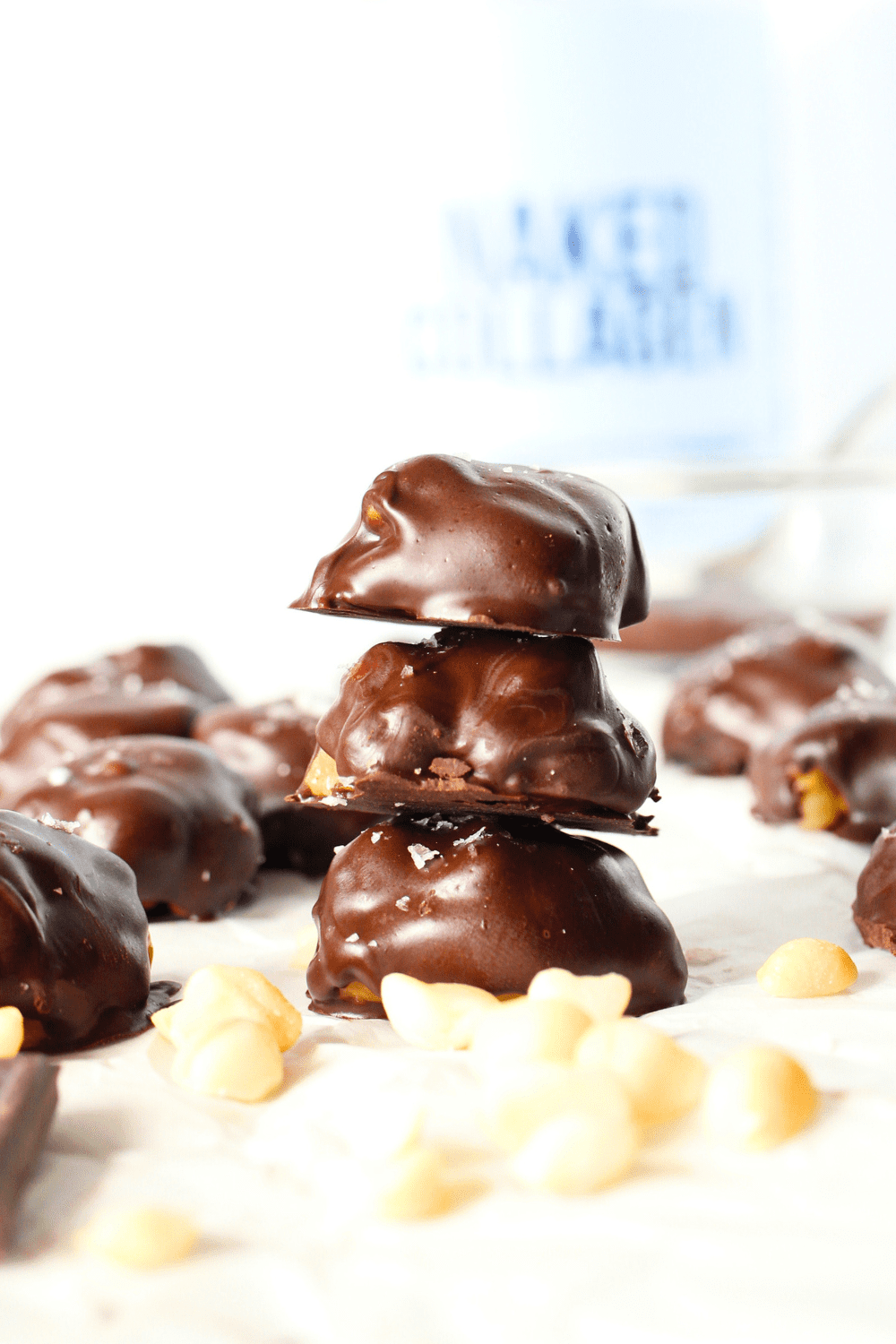 front view of 3 copycat macadamia caramel clusters stacked on top of each other with macadamia nuts scattered around and collagen protein powder in the background