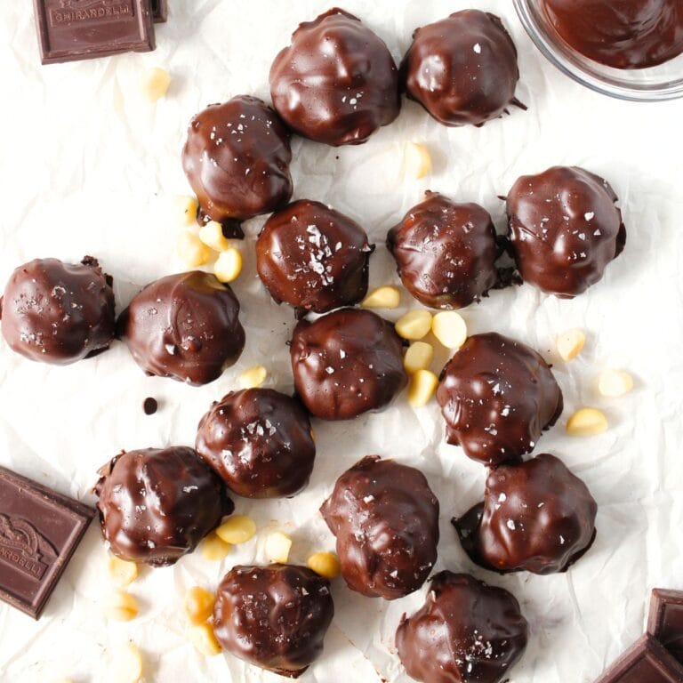 top view of keto chocolate macadamia caramel clusters on a sheet of parchment with scattered macadamia nuts and sugar-free bits of chocolate
