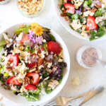 top view of two bowls of keto strawberry poppyseed salads that are copycat versions of Panera bread with lettuce, chicken, sugar-free poppyseed dressing, nuts and crumbled blue cheese. 2 forks sit besides the salad bowls.