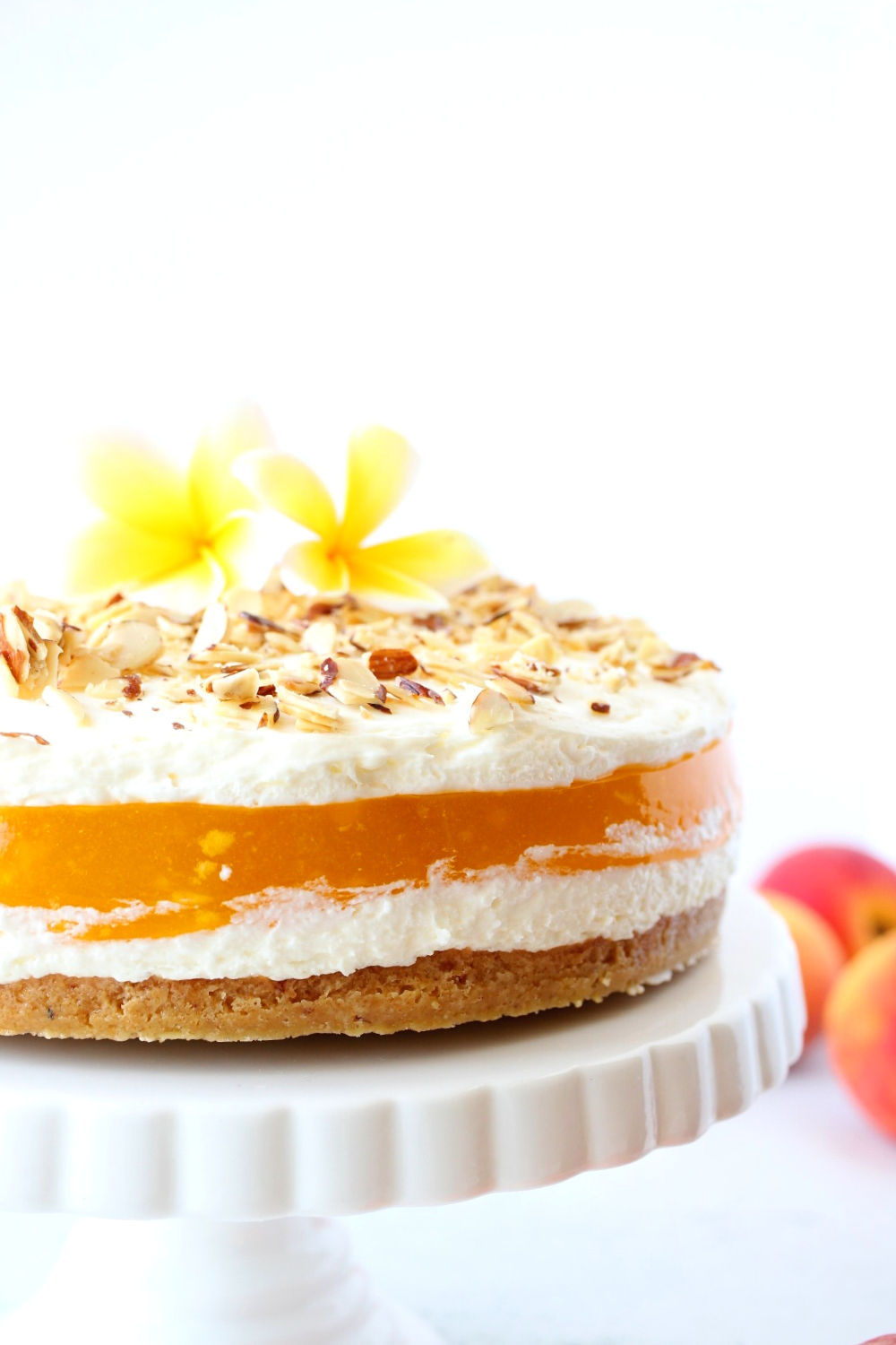 keto peaches and cream pie with flowers on top on a cake stand