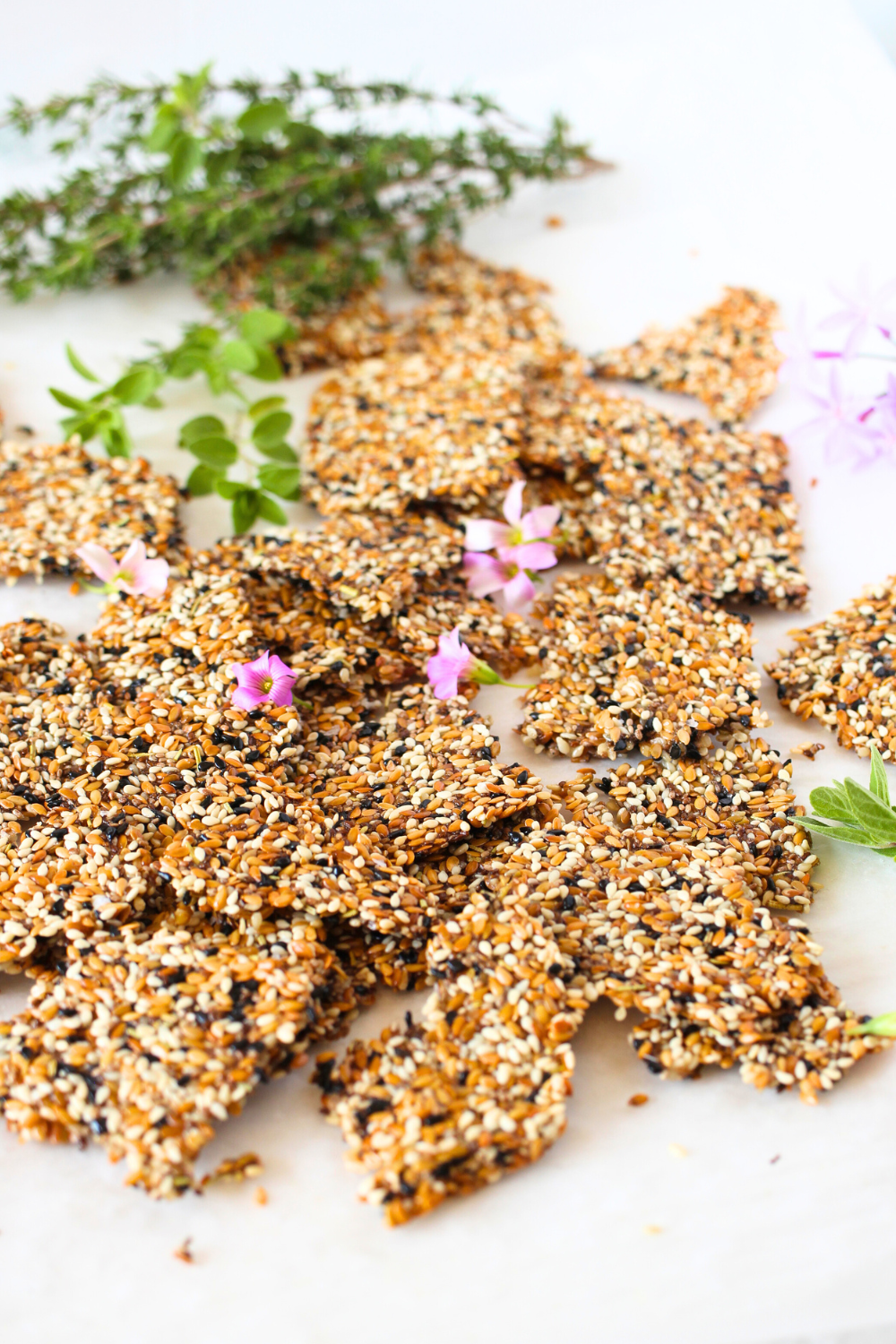 Angular vew of plant-based keto seed crackers broken into individual crackers with herbs and chive flowers