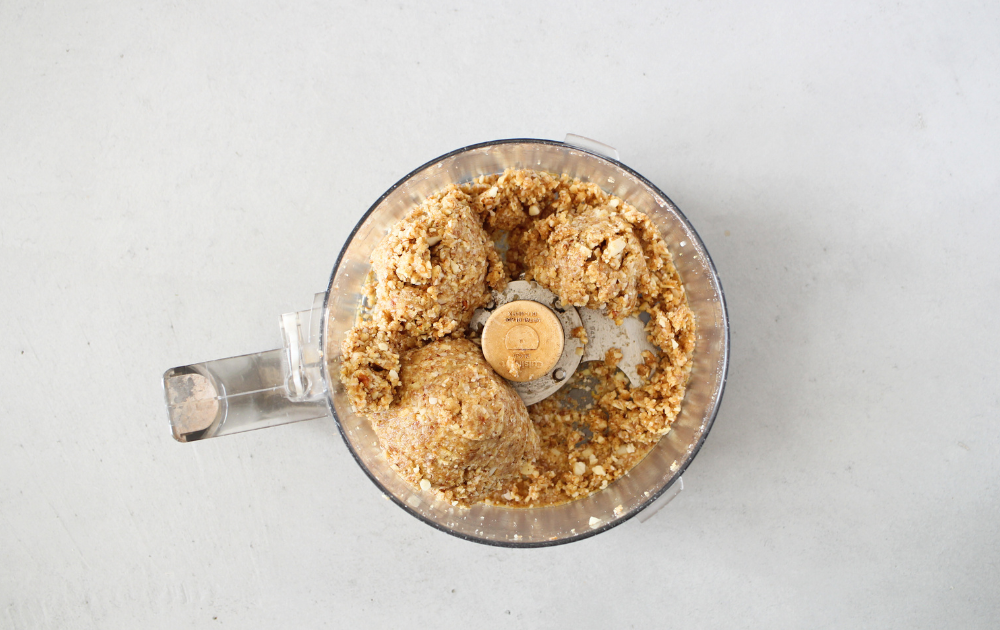 top view of the food processor with ground nuts and liquid ingredients thoroughly combined and sticking together to form a ball.