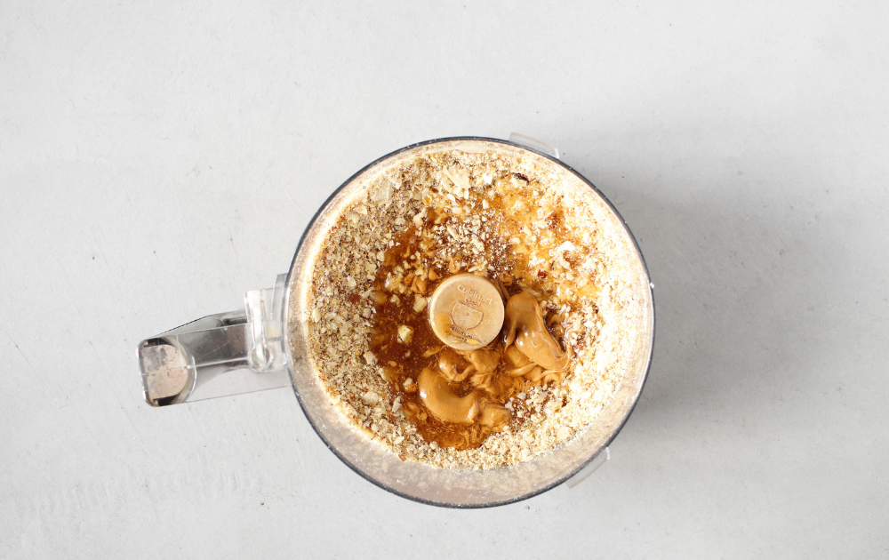 top view of a food processor with ground nuts and tapioca fiber, nut butter and honey over the ground nuts