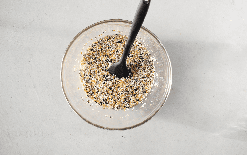 top view of a bowl containing the nut-free keto cracker ingredients made up of seeds and boiling water with a black mixing spoon
