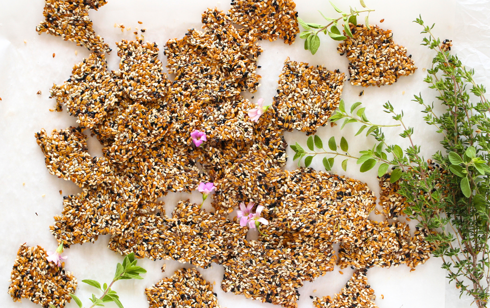 top view of plant-based keto seed crackers broken into individual crackers wtih herbs and chive flowers