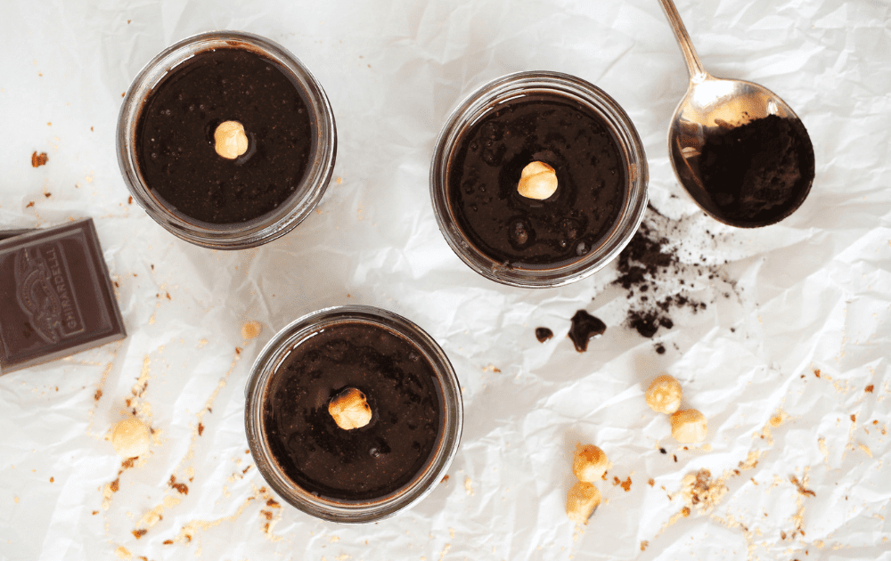 top view of homemade keto espresso nutella in mason jars with a roasted hazelnut on top and cocoa powder on the side.