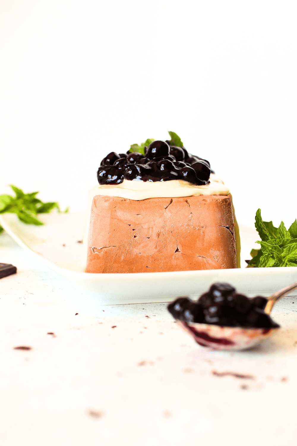 a front view of the keto chocolate semifreddo with melted sugar-free white chocolate and sugar-free blueberry pie filling on top.  Mint is scattered throughout with a spoon filled with blueberry pie filling