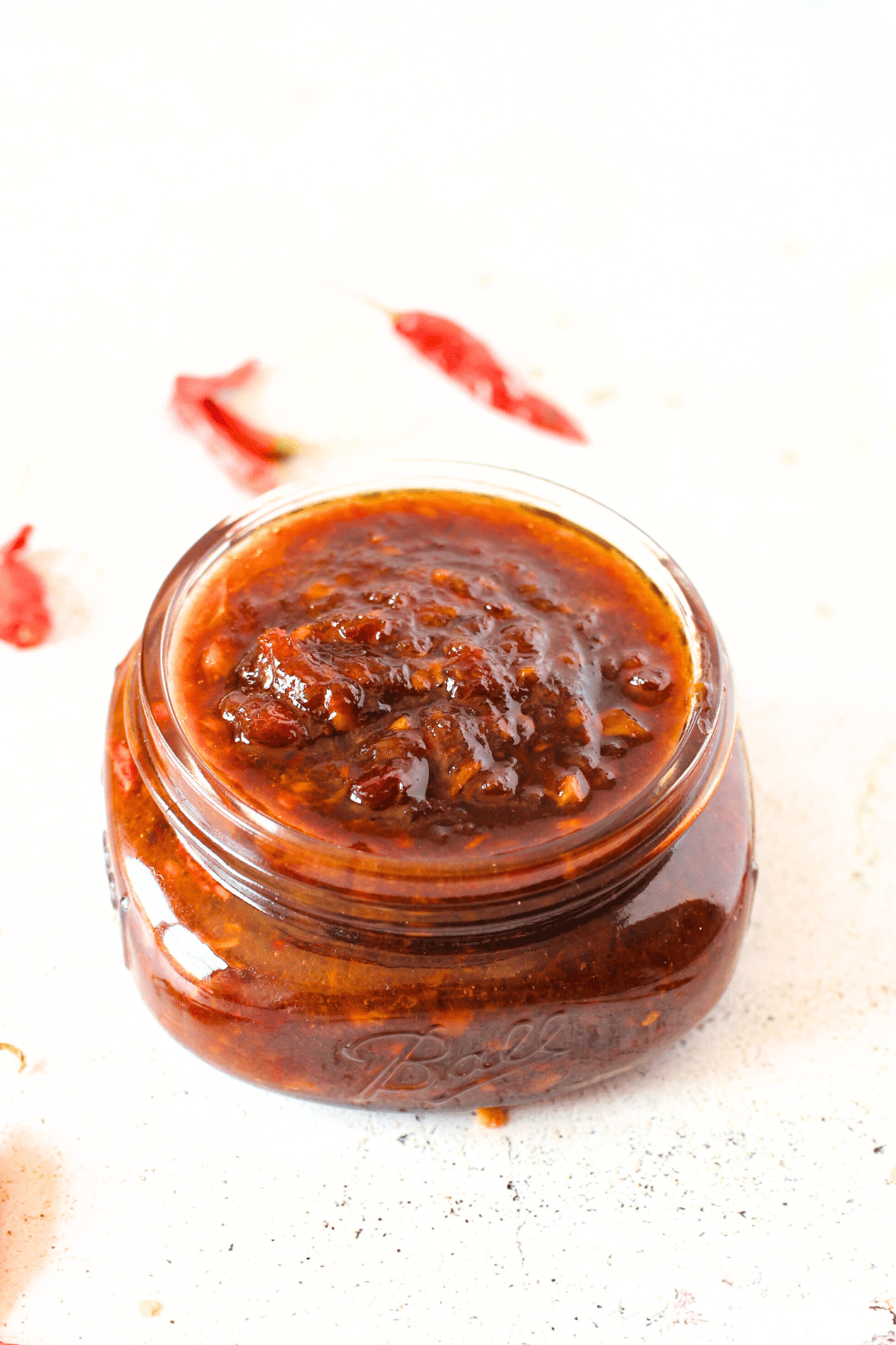 a top view of a mason jar filled with a keto thai chili jam and arbol dried peppers scattered around the jar.