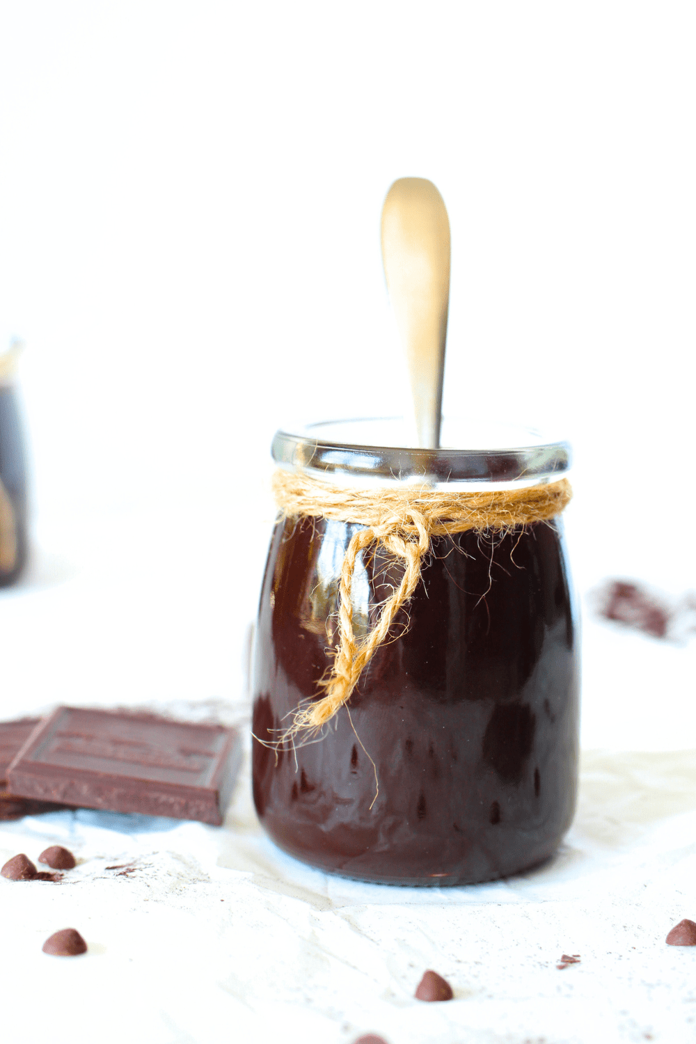 front view of a jar of sugar-free chocolate fudge sauce wtih a spoon and unsweetened chocolate scattered around the jar