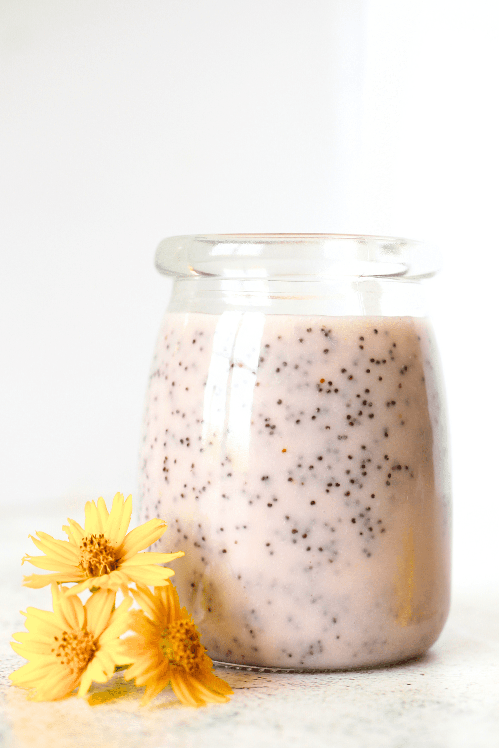 front view of a jar filled with easy keto poppy seed dressing and yellow flowers beside the jar