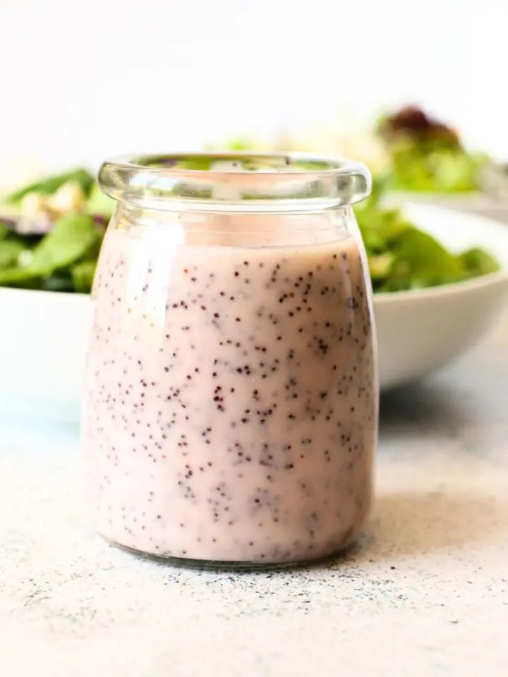 front view of a jar of easy sugar-free poppy seed dressing with a salad in a bowl behind the jar.