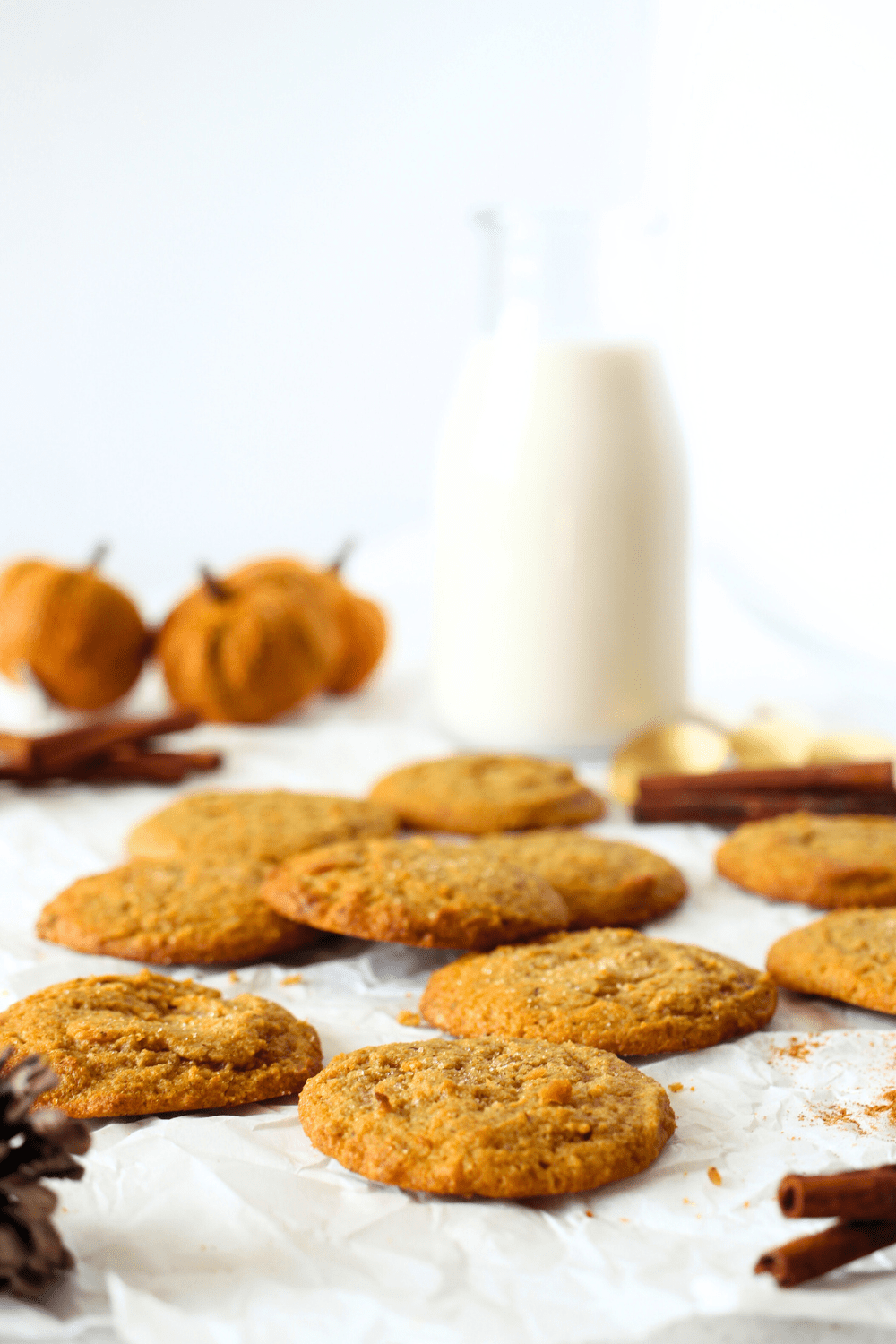 baked chewy keto pumpkin cookies with cinnamon and jug of milk.  Pumpkins are scattered in the background