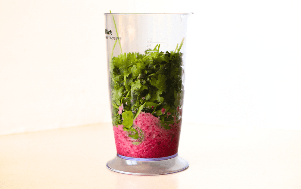 side view of a stick blender cup with pureed red onion and vinegar mixture in the bottom and the fresh mixed herbs on top