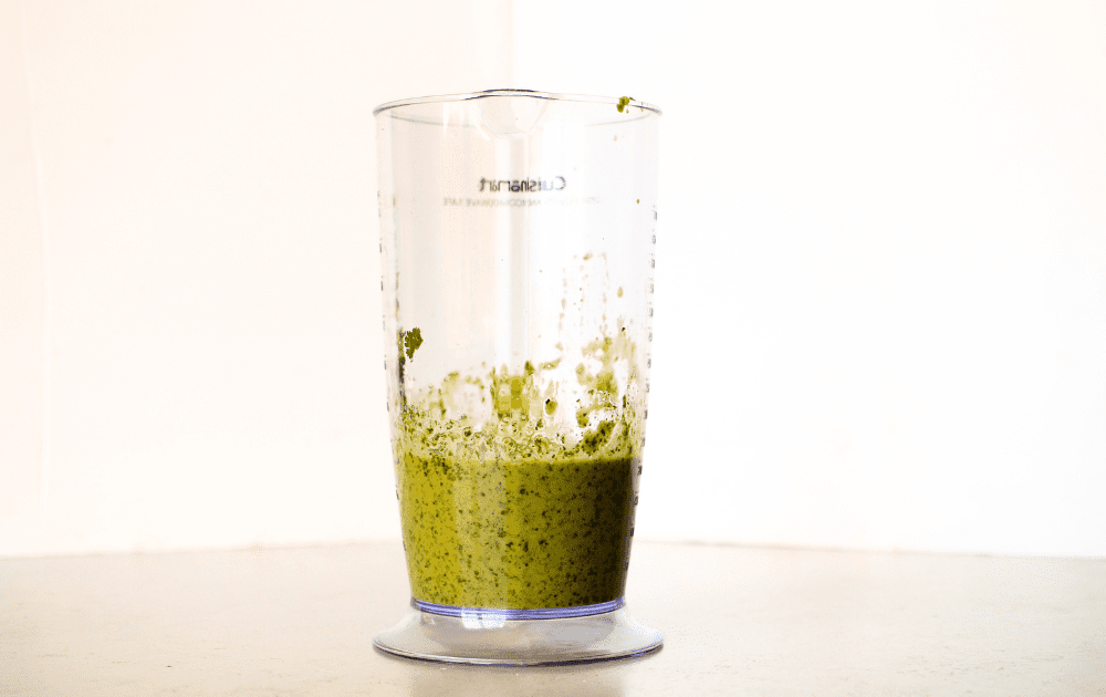 side view of a cup from an immersion blender with pureed fresh herbs to make a keto herb dressing