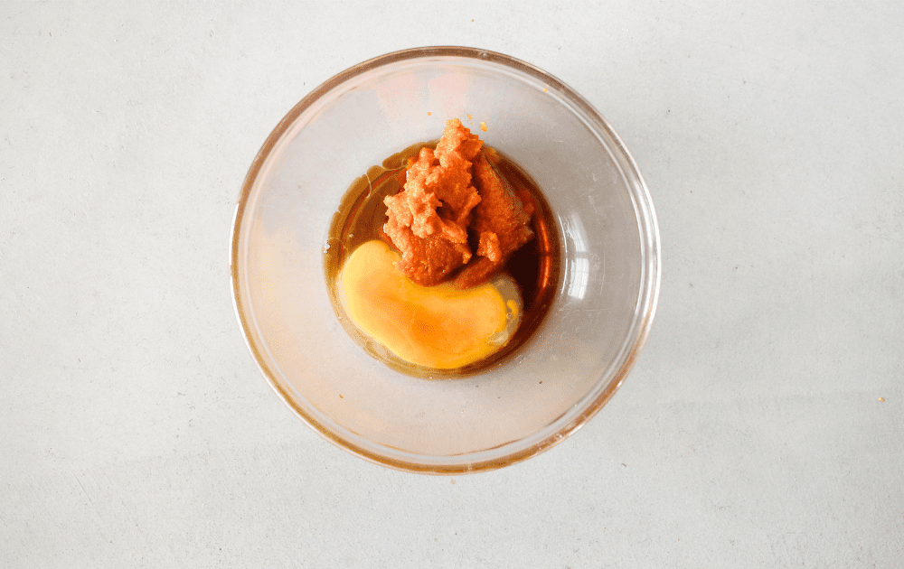 top view of a mixing bowl with an egg, pumpkin puree and vanilla before being whisked together to make keto chewy cookies