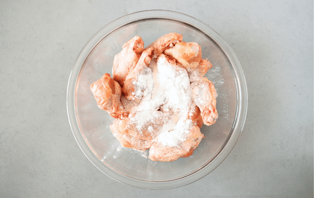 top view of a mixing bowl with paper towel dried wings being tossed in baking powder to make the wings nice and crispy