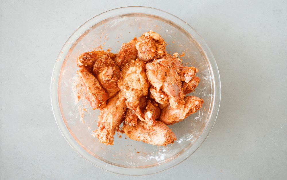 top view of a bowl of raw chicken wings being tossed with Cool Ranch seasoning which includes Hidden Valley Ranch powder, garlic, onion, salt and smoked paprika