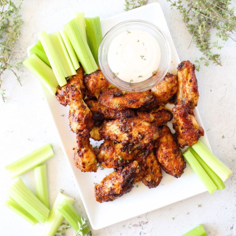 a plate filled with baked chicken wings made in an air fryer and seasoned with ranch dressing. Celery sticks and extra ranch dip are served alongside the keto wings