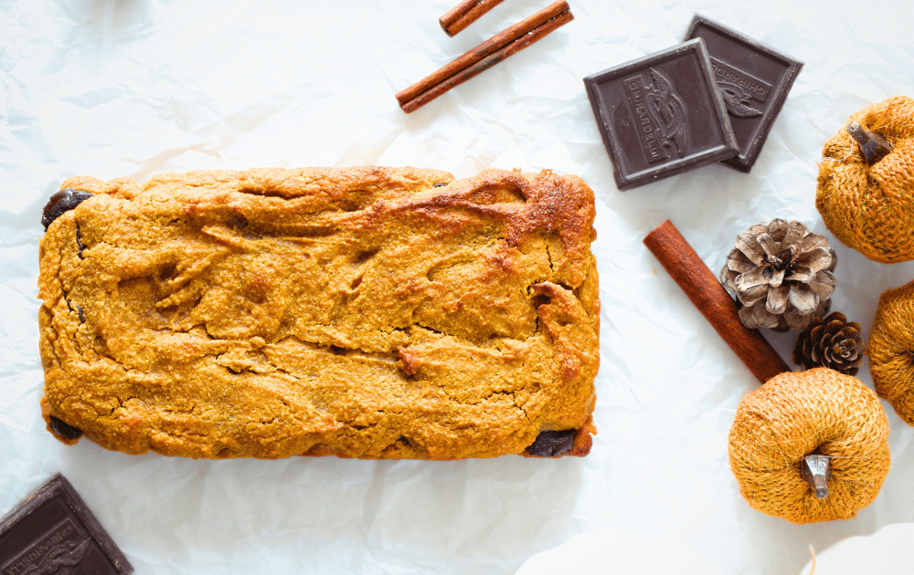 top view of sugar-free pumpkin bars with a chocolate layer after being baked.  chocolate squares and cinnamon sticks surround the keto pumpkin chocolate bars