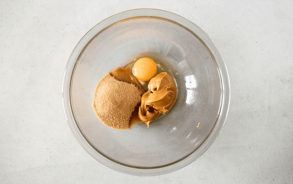top view of a glass bowl with peanut butter, egg and sugar-free brown sweetner to make keto pumpkin chocolate bars
