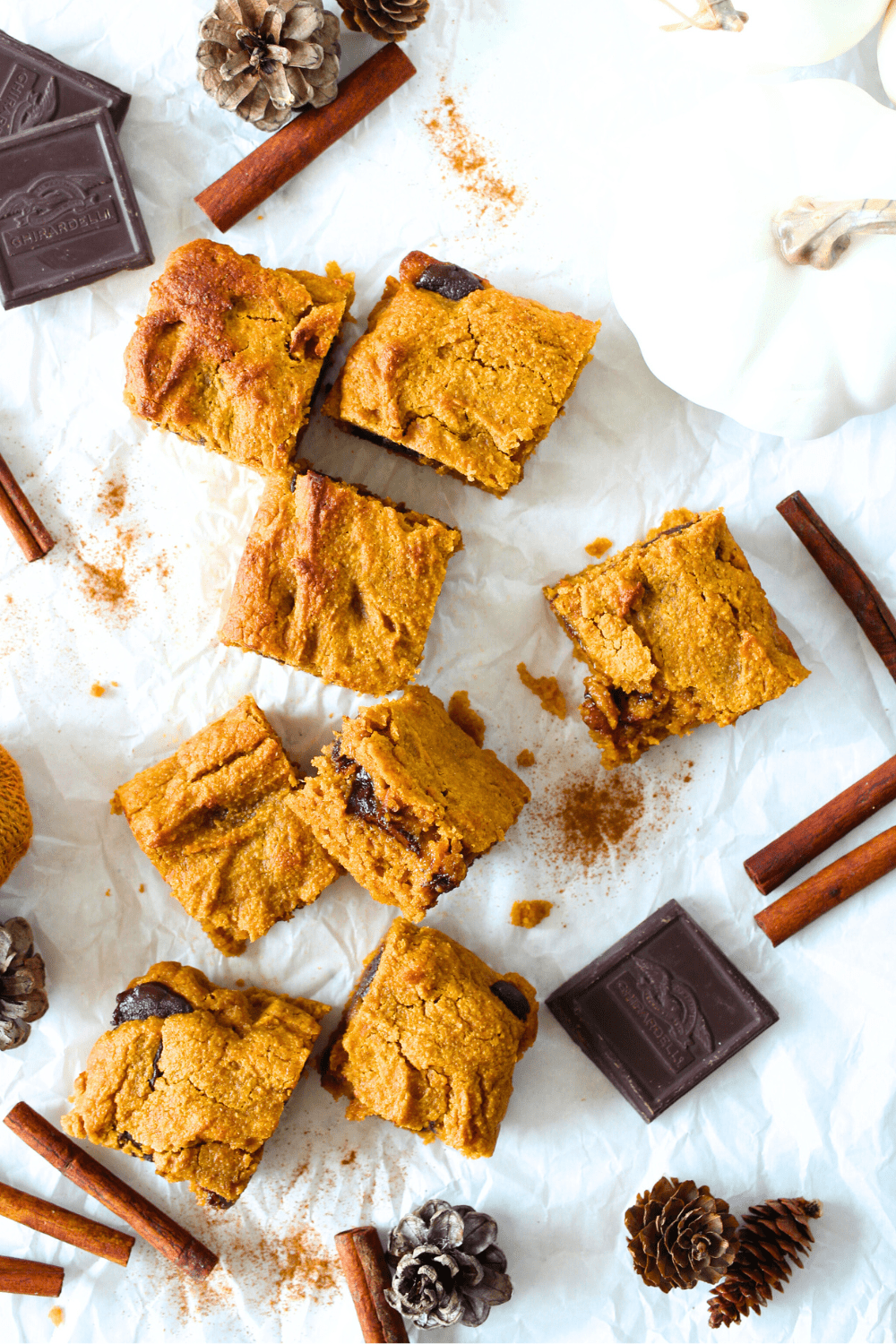 top view of easy keto pumpkin bars scattered on a table with sugar-free chocolate, cinnamon and fake pumpkins lying around