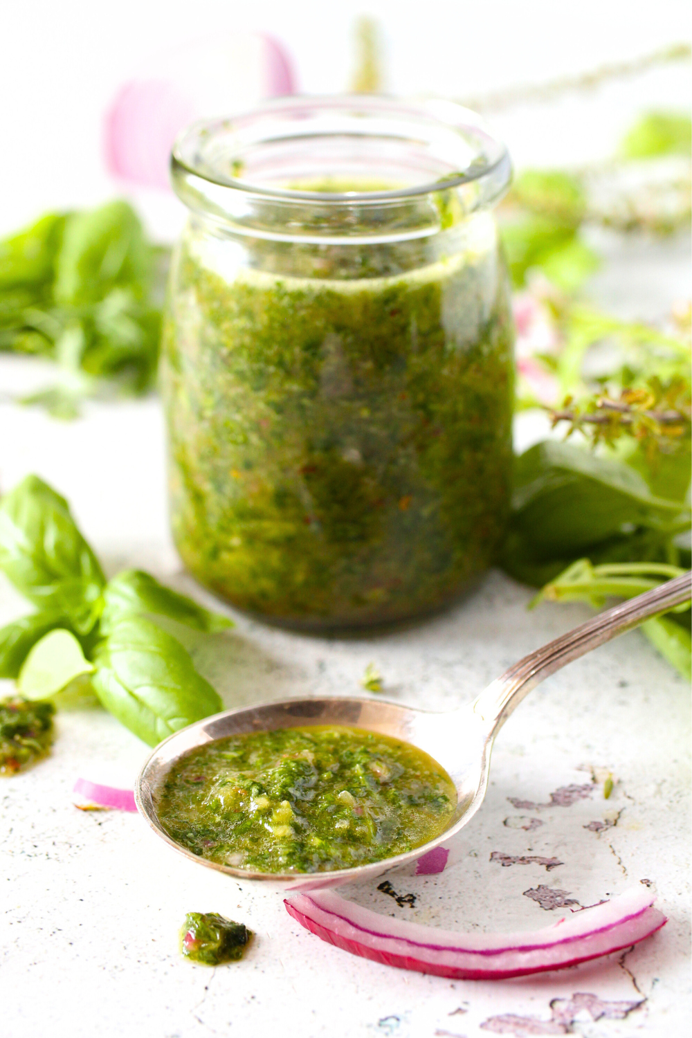 a spoon with healthy keto fresh herb dressing. A jar of the keto salad dressing is in the background with leftover herbs and red onion