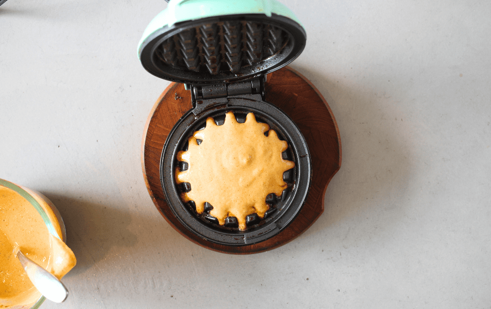 top view of a Dash mini waffle maker with keto pumpkin waffle batter poured into the mini waffle maker