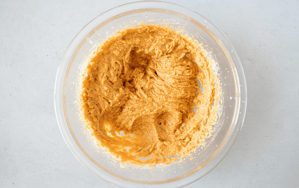 top view of a mixing bowl with almond flour, pumpkin, sugar-free sweetener, spices and whey protein powder after being beaten together to form a keto pumpkin cake