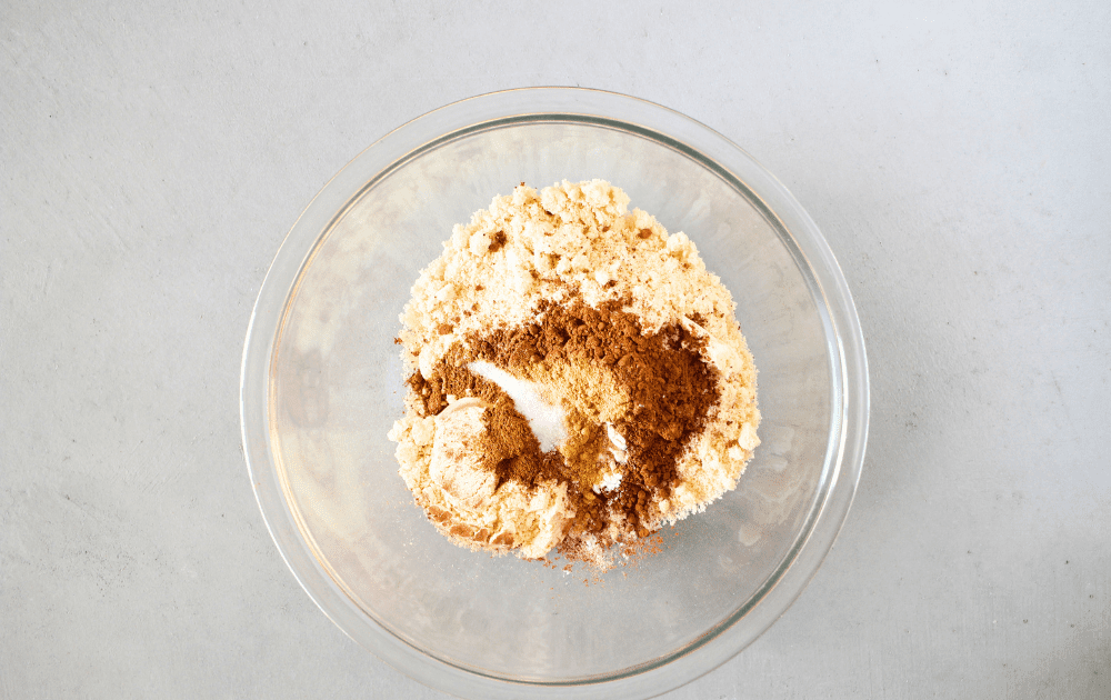 top view of a mixing bowl with almond flour, whey protein powder, cocoa powder, pumpkin pie spice, ginger, cardamom, baking soda, baking powder and salt before being whisked together to make the keto pumpkin gingerbread recipe