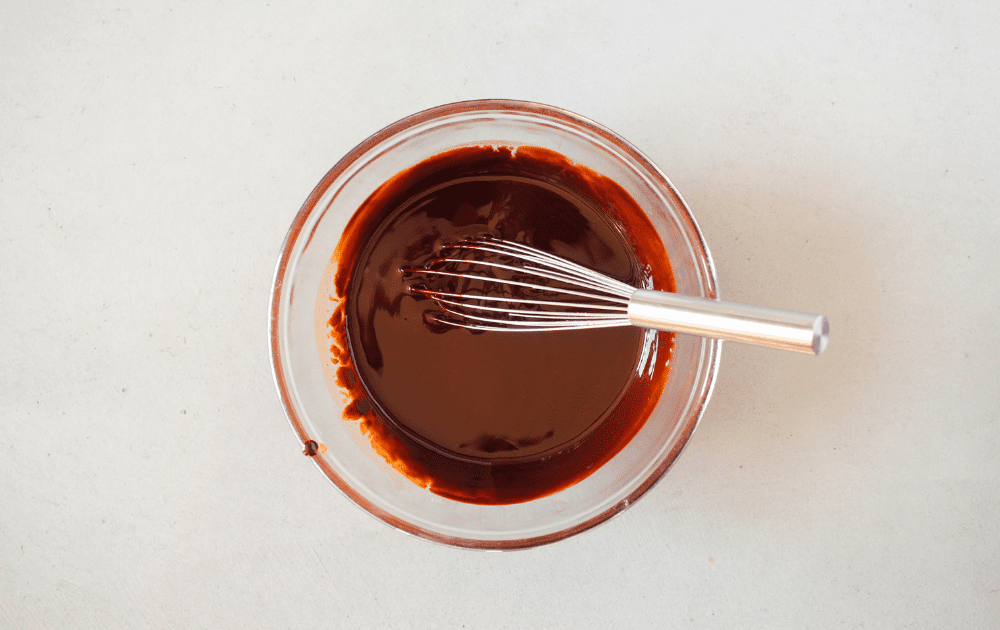 top view of a mixing bowl with melted butter and melted sugar-free chocolate whisked together with a metal whisk.