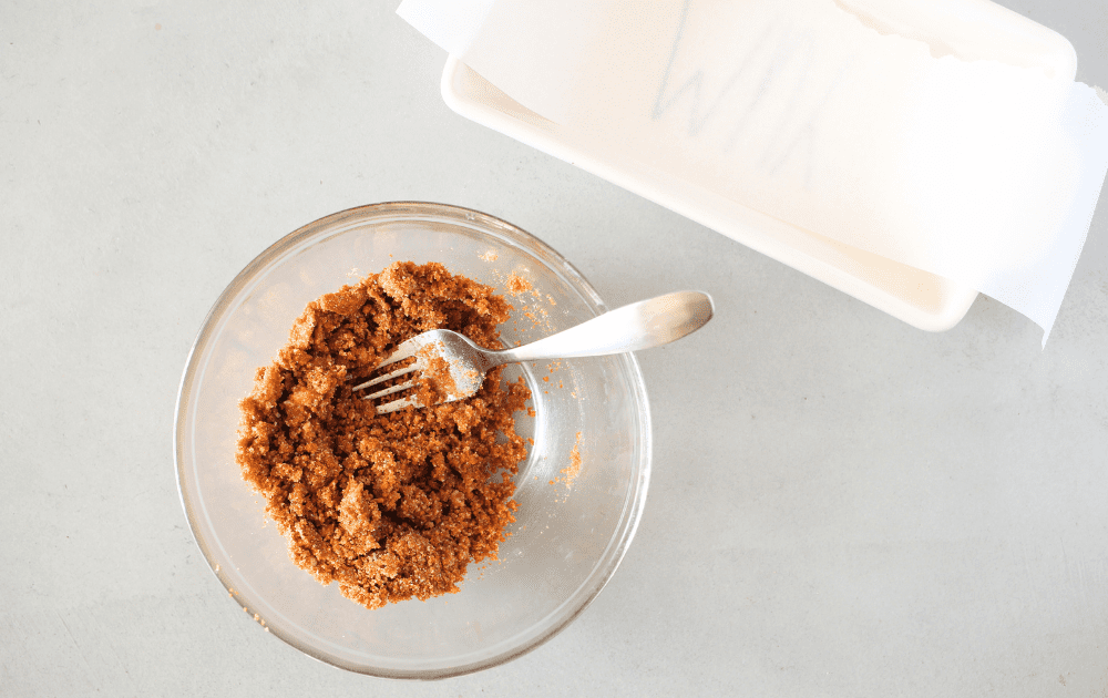 top view of a loaf pan lined with parchment paper and a bowl with a fork that has mixed together almond flour, melted butter, pumpkin pie spice and salt.