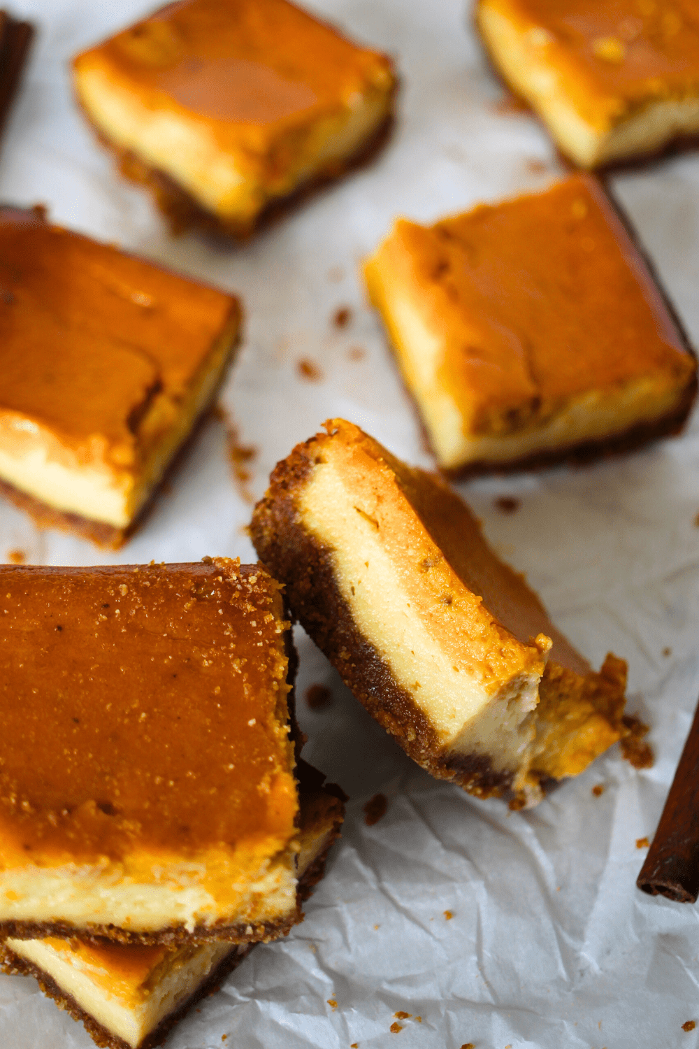 sugar-free pumpkin cheesecake bars scatterred around with one bar lying on its side to show the keto cheesecake bar layered on top of the keto pumpkin bar
