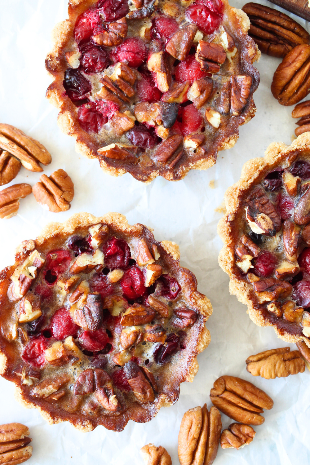 top view of a keto pecan cranberry tart with additional keto pecan tarts and pecans scattered about