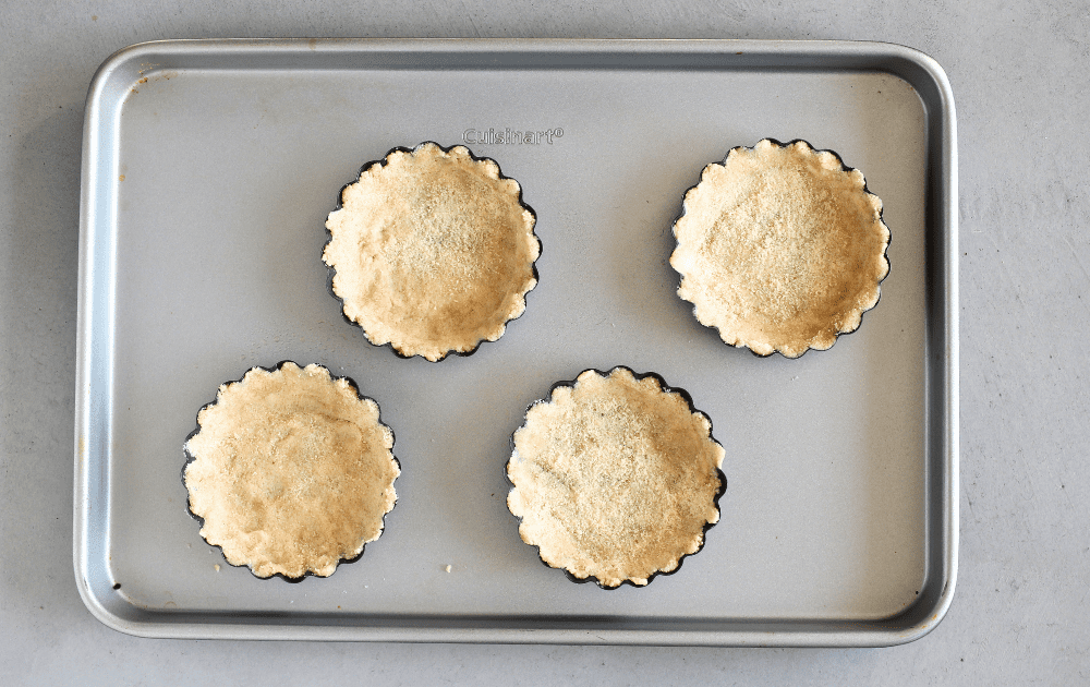 top view of 4 mini tart pans with keto tart crust pressed into each mini tart set on a rimmed baking sheet