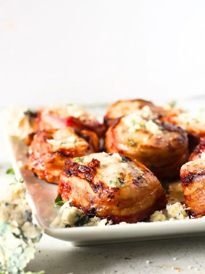 a white plate loaded with keto bacon-wrapped pork with crumbled blue cheese and fresh herbs
