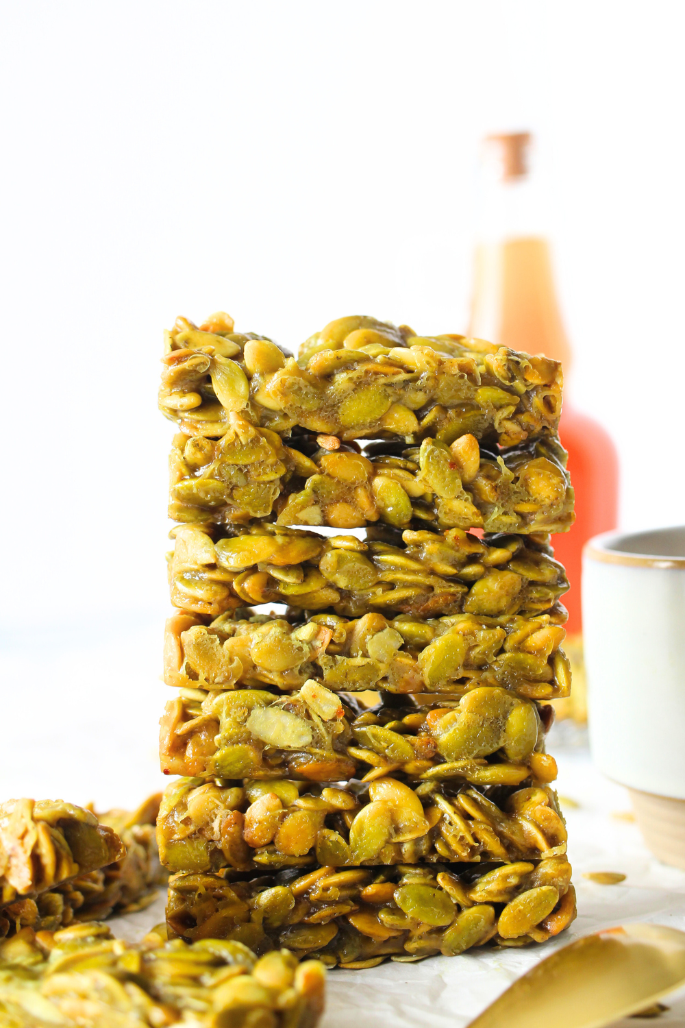 keto copycat warrior bar made with pumpkin seeds stacked on top of each other with a cup of coffee and pumpkin seeds scattered around the keto pumpkin seed protein bars