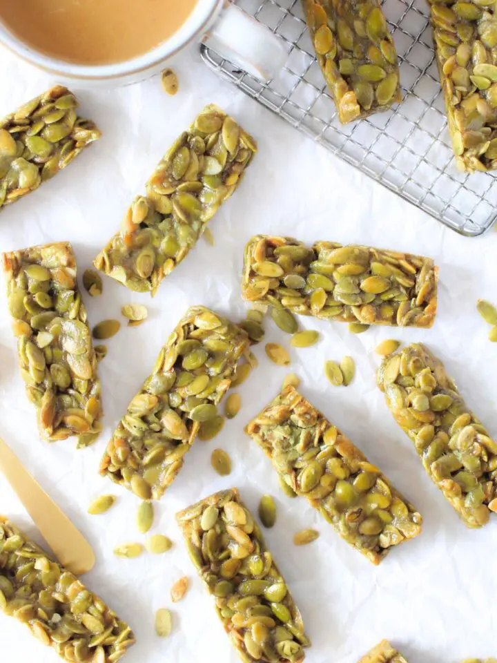 sugar-free protein bars made with pumpkin seeds scattered with a cup of coffee and sugar-free syrup