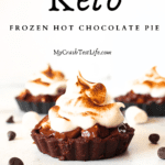 keto hot chocolate frozen pies with torched sugar-free marshmallow fluff frosting. Sugar-free chocolate chips and sugar-free marshmallows are scattered around the mini tarts