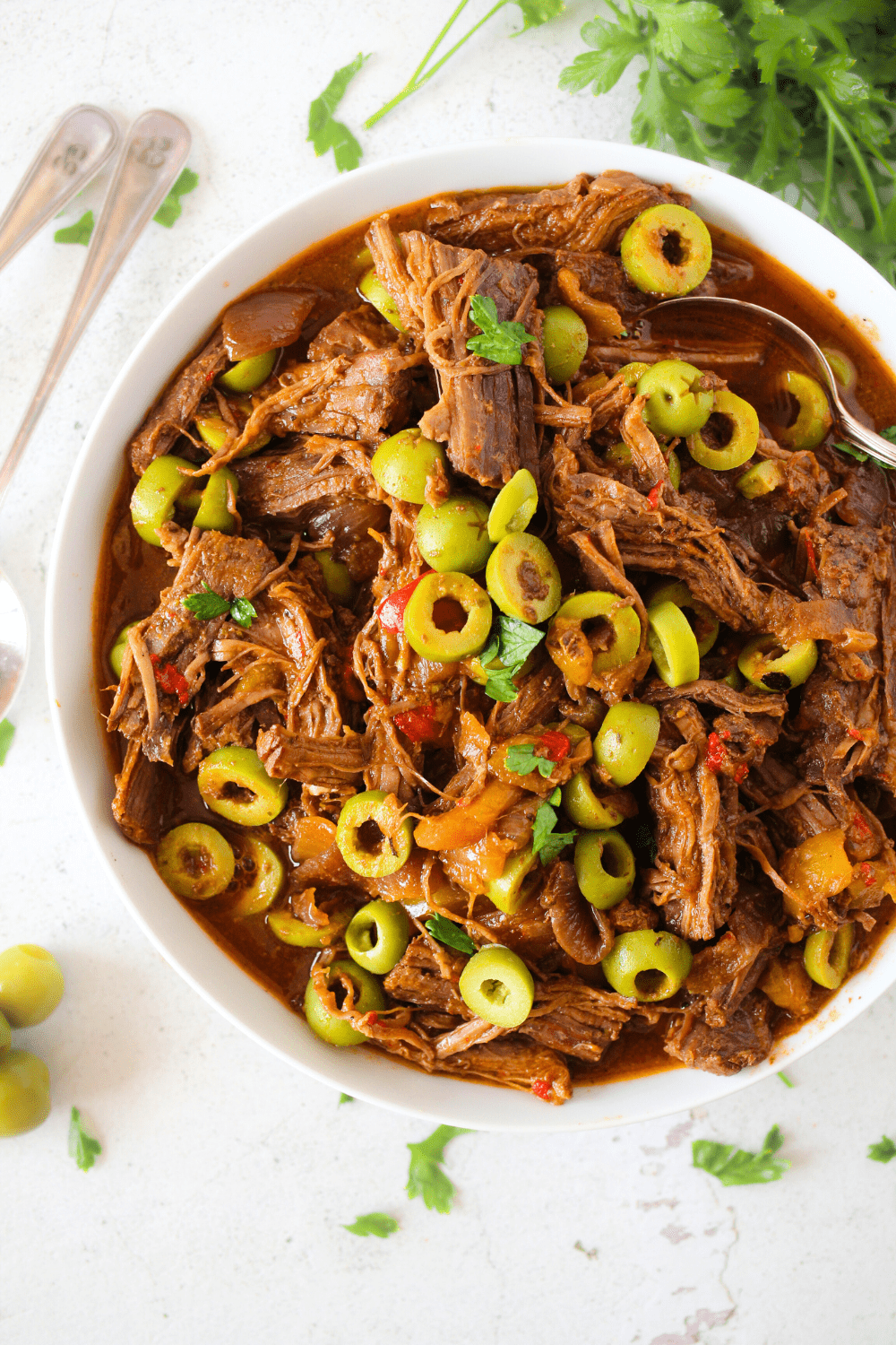 a white bowl with keto slow cooker Cuban beef stew with onions, peppers and olives with 2 spoons