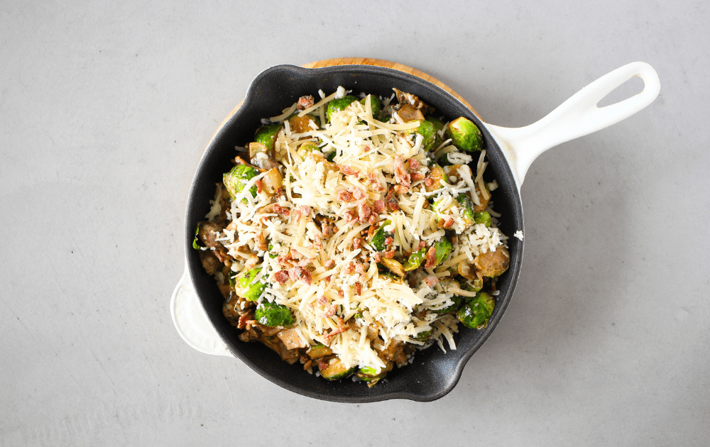 top view of a skillet filled with keto cheesy Brussels sprouts and topped with more cheese before being baked