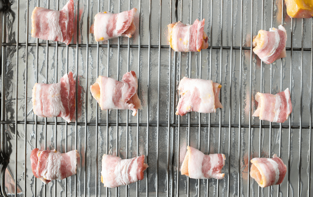 top view of a grilling sheet with chicken wrapped in bacon before being baked for an easy keto appetizer
