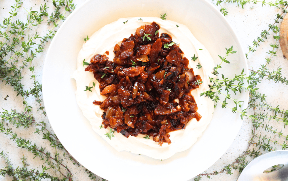 top view of a white bowl with keto whipped goat cheese and bacon jam on top with sprigs of thyme scattered around