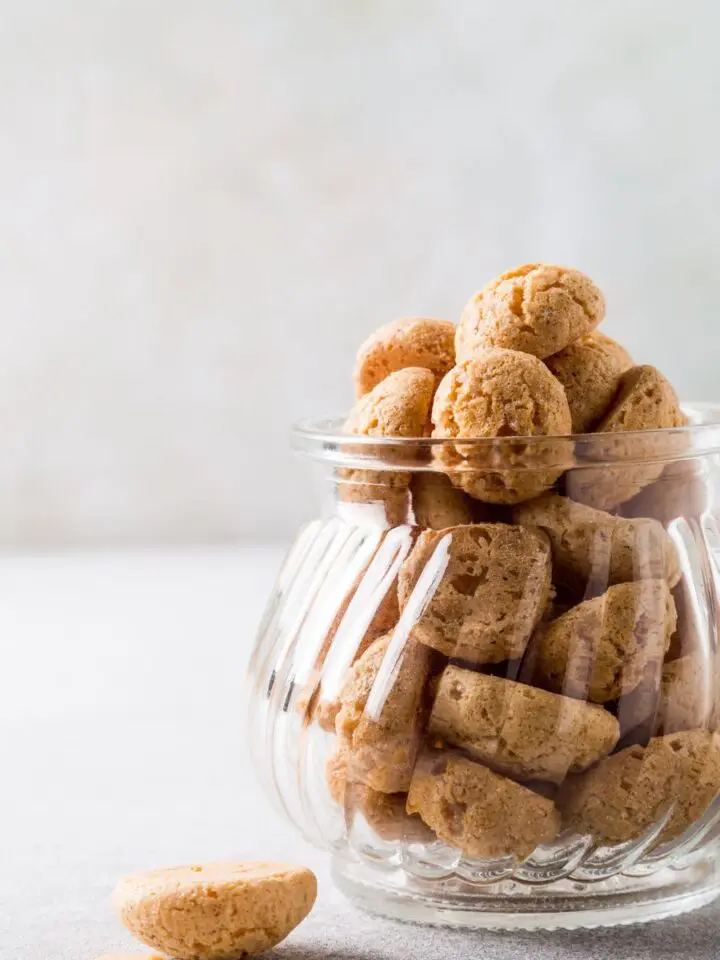 a glass jar filled with keto amaretti cookies with a cup of coffee in the background