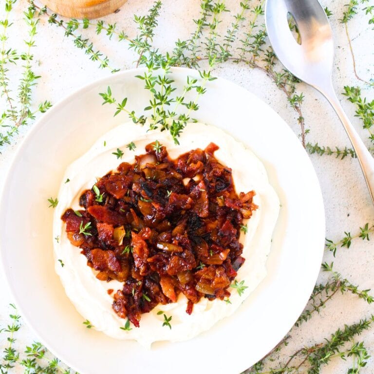 a white bowl loaded with keto whipped goat cheese and bacon jam on top with fresh thyme scattered around the bowl