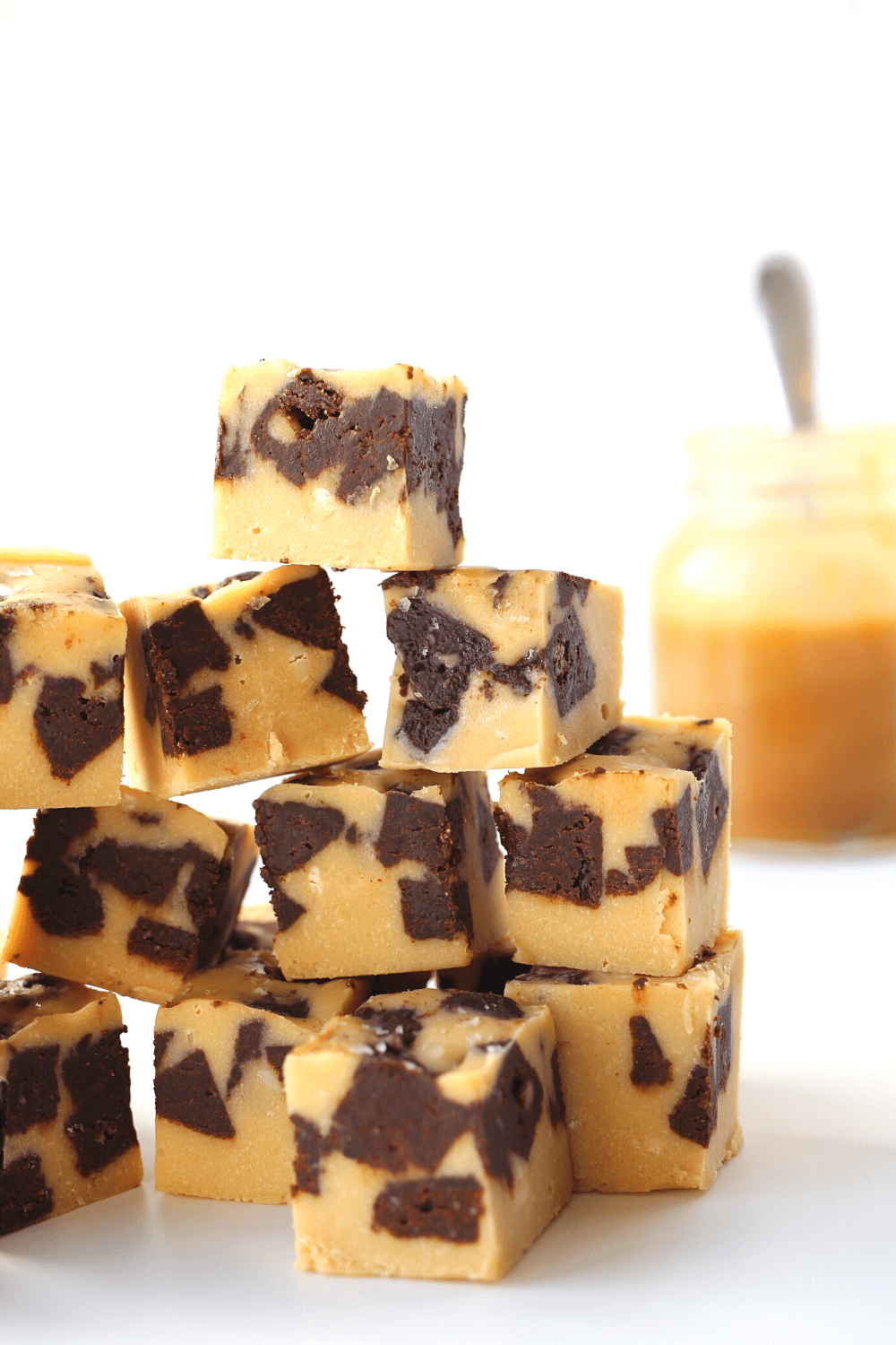 keto satled caramel brownie fudge stacked on top of each other with sugar-free caramel sauce in the background