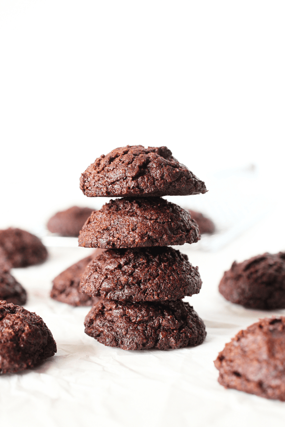 a stack of small-batch fudgy keto chocolate cookies stacked on top  of each other with remaining sugar-free chocolate cookies in the background.