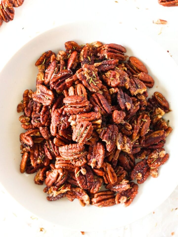 top view of a bowl of keto rosemary brown butter nuts with nuts scattered around the bowl along with herbs